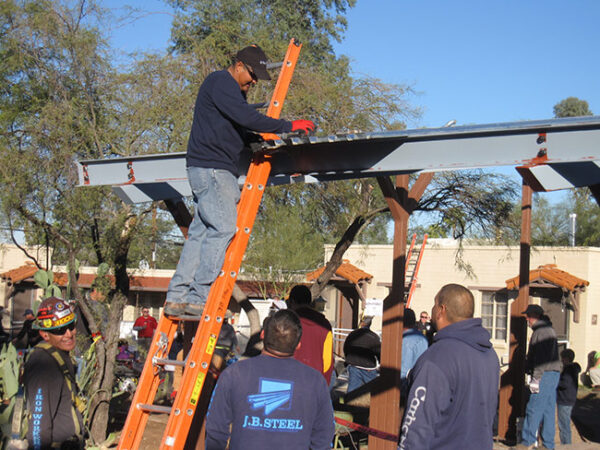 Volunteer on a ladder assisting the the installation of a metal roof on an open shelter during the 2013 Arizona Builders Alliance Volunteer Day.